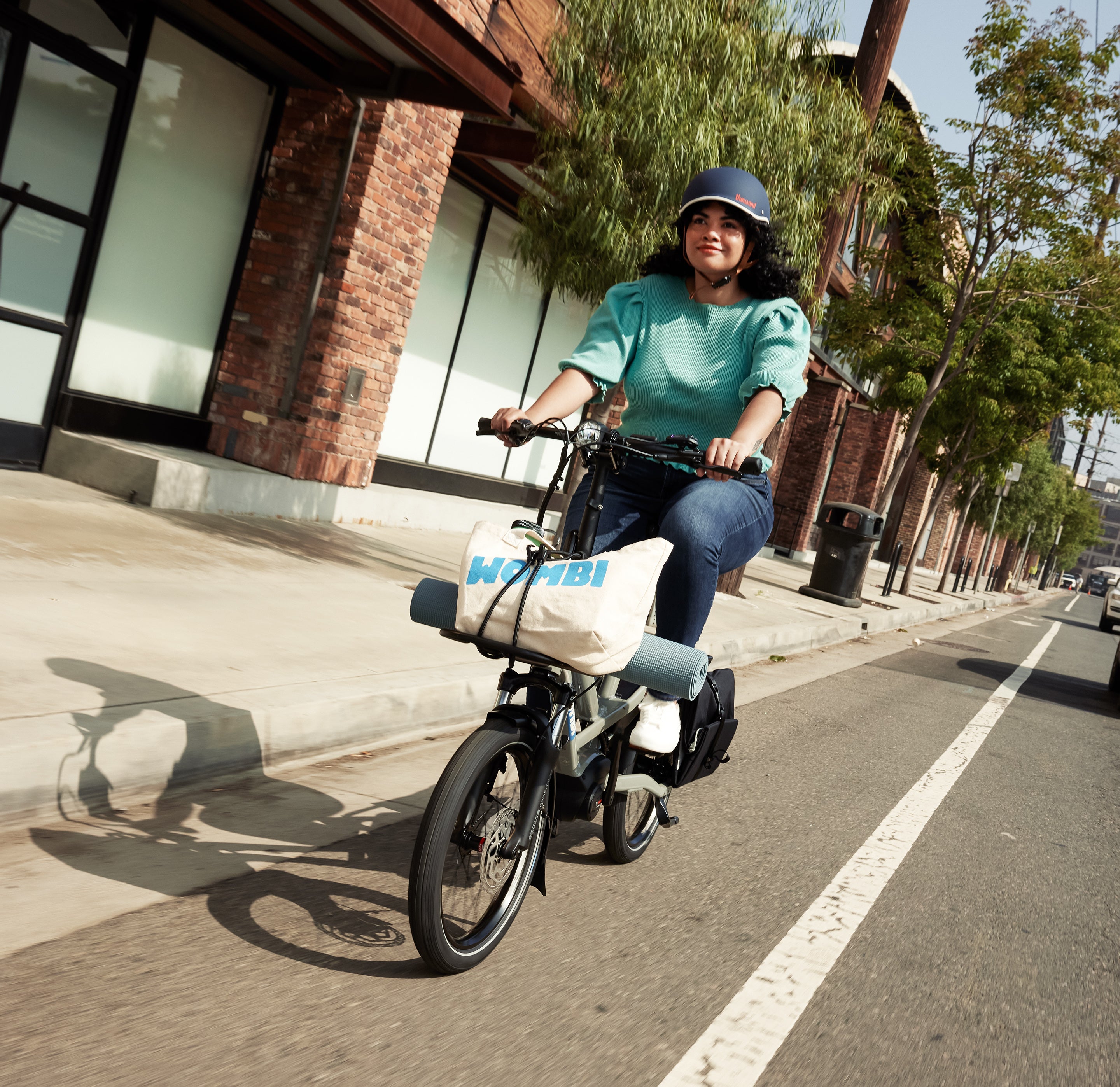 Person riding a HSD Tern electric bicycle with a Wombi bag on a city street.